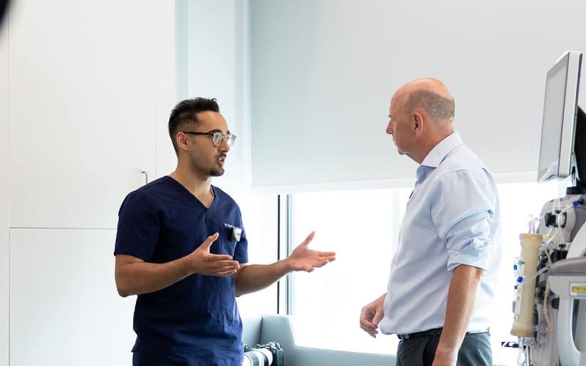 Dr Dev Gakhar in scrubs talking with a colleague on a hospital unit